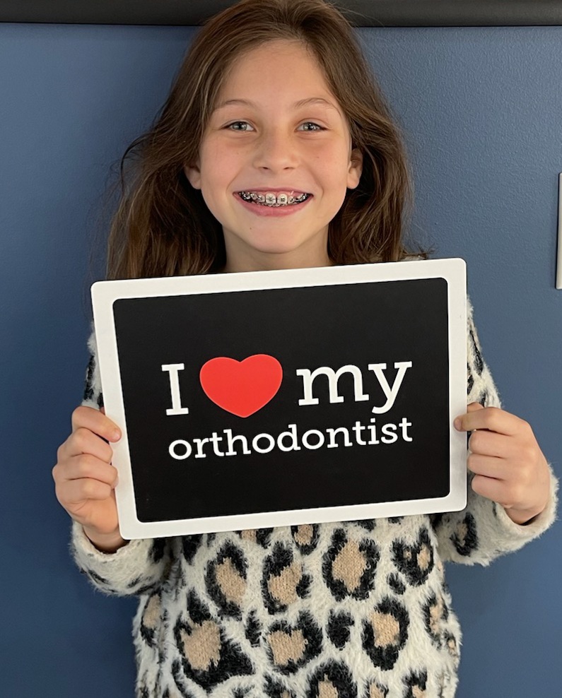 A young patient with braces holding an I love my orthodontist sign